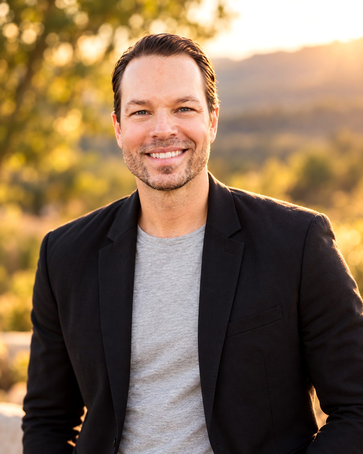 Dominic Bartola smiling outdoors in a black blazer and gray shirt