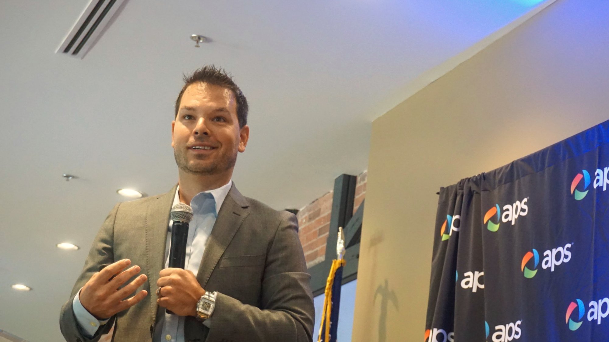Dominic Bartola speaking into a handheld microphone at an APS event