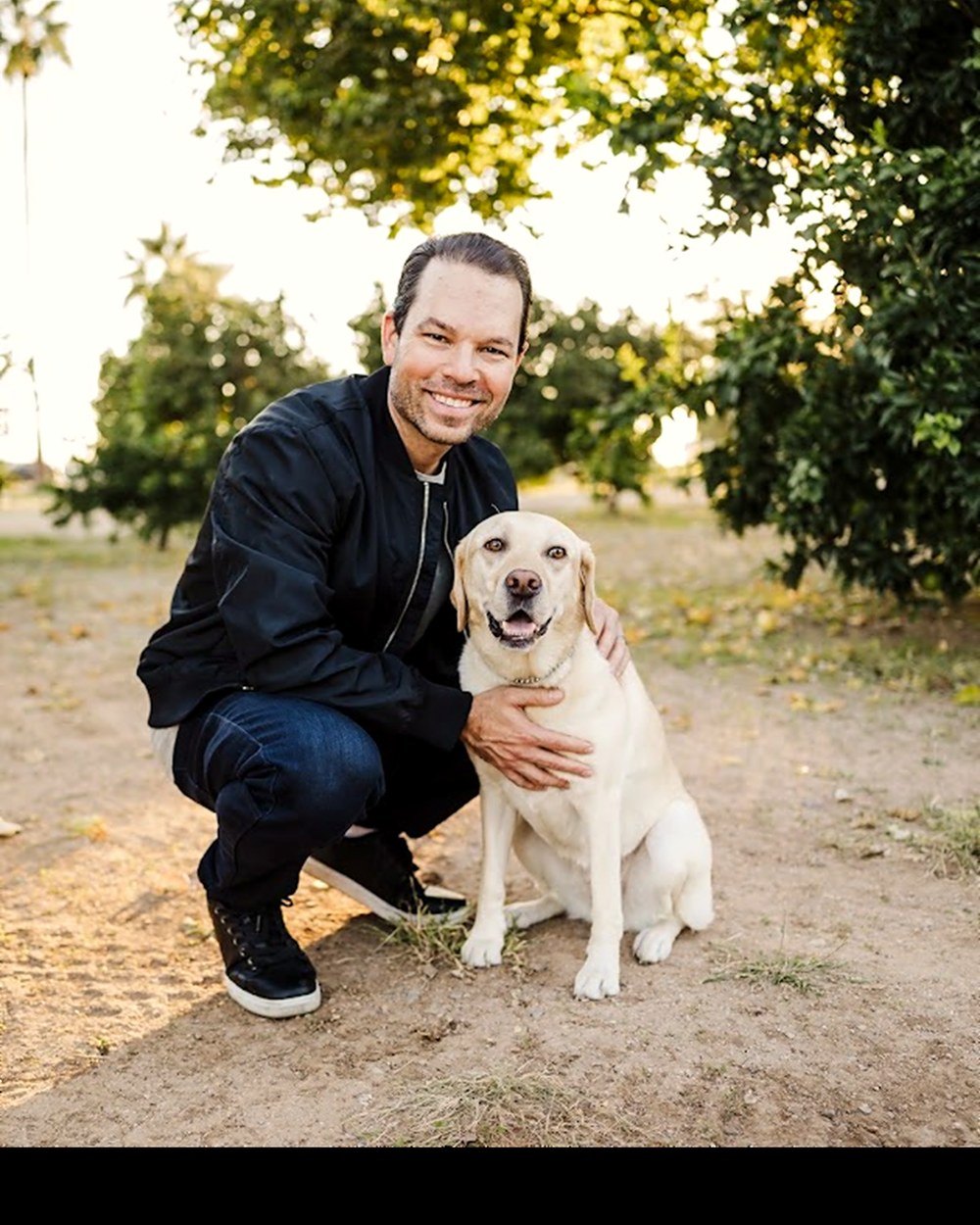 Dominic Bartola crouching beside his yellow Labrador hearing dog outdoors